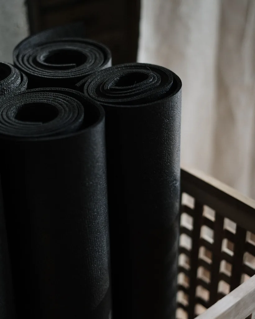 Esterillas de yoga enrolladas y ordenadas dentro de una cesta de madera junto a la pared de la sala